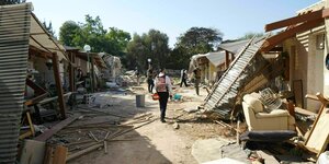 Auf der Straße zwischen den Häusern des zerstörten Kibbuz liegen Möbel, zersplittertes Holz - Menschen sind auf dem Weg zu sehen