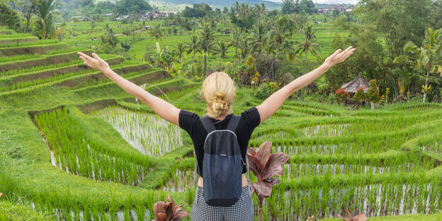 Ein junge Frau mit ausgebreiteten Armen in einem Reisfeld