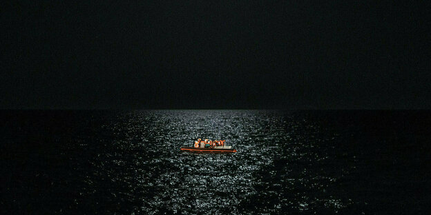 Ein kleines Boot gefüllt mit Personen in Rettungswesten in tiefer Nacht auf See