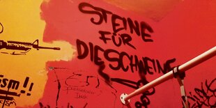 Auf einer roten Wand steht mit schwarzer Schrift "Steine für die Schweine".