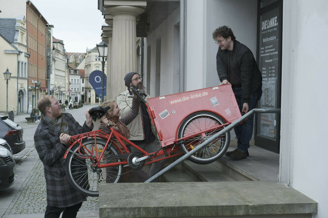 Vier Menschen heben ein rotes Wahlkampf-Lastenrad der Linken eine Treppe hoch