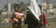 Ein mann mit einem baby im Arm, eine Frau, die ein weißes T-shirt als Fahne verwendet und ein wietrere Mann auf den Straßen von gaza