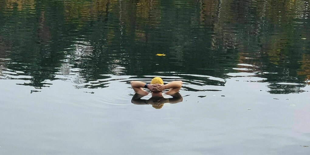 Eine Person mit Badekappe schwimmt im November in einem See