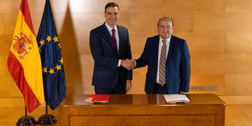 Die Flagge Spaniens und Europas stehen in der Ecke. Handschlag zwischen Pedro Sanchez und Andoni Ortuzar (Präsident der baskischen Partei PNV)