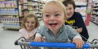Ein Kind sitzt im Einkaufswagen, lacht und wird von zwei Freund:innen angeschoben