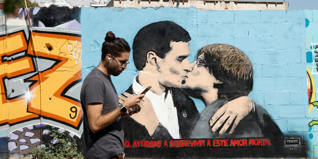 Ein Mann geht in Barcelona an einem Wandbild vorbei, auf dem Pedro Sanchez und Charles Puigdemont sich küssen