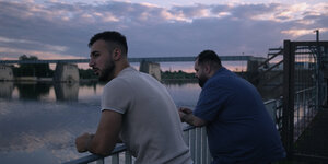 Zwei Männer blicken über ein Geländer auf einen Fluss