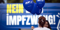 Eine Frau hält blaue Luftballons in der Hand mit der Aufschrift Auf1 - im Hintergrund ist ein Plakat zu sehen: Kein Impfzwang