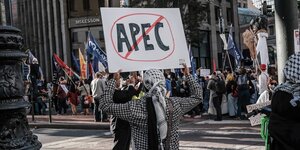 Eine Person mit PaliTuch um den Kopf hält ein Schild hoch, auf dem die Aufschrift APEC durchgestrichen ist