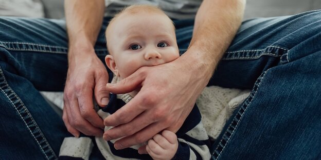 Ein Baby beißt in die Hand seines Vaters