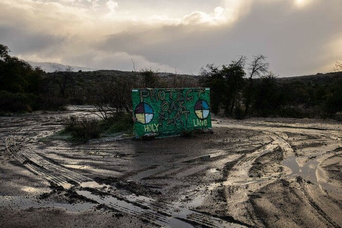 "Protect Oak Flat" und "Holy Land" steht auf einem Schild das inmitten einer Schlammfläche steht, drumherum sind Reifenspuren zu sehen