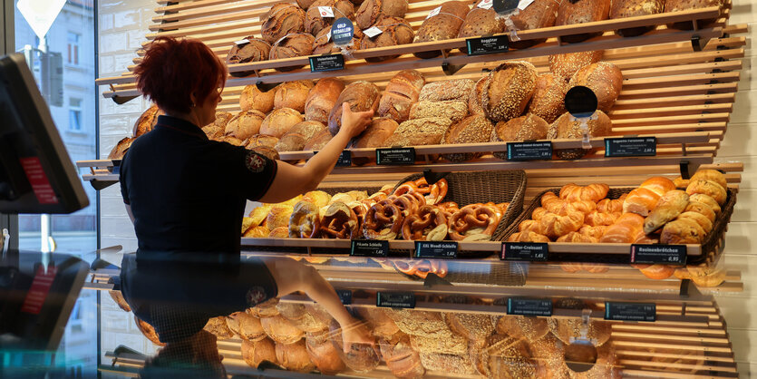 Eine Mitarbeiterin räumt Mischbrot in die Auslage einer Bäckerei.