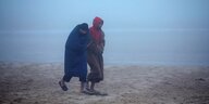 Zwei Männer, die in Decken gehüllt sind an einem nebeligen Strand