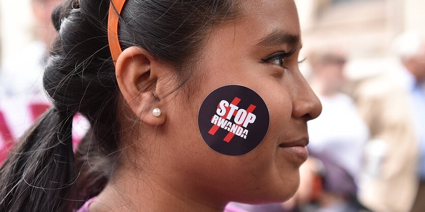 Ein Mädchen hat sich einen Aufkleber auf die Wange geklebt, darauf steht "Stop Rwanda"