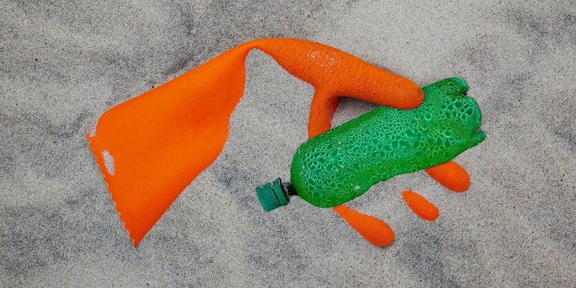 Plastikhandschuh und Plastikflasche im Sand