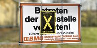 Schild an Zaun "Betreten der Baustelle verboten" mit Protestaufkleber "X"