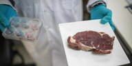 Ein zerklüftetes Steak neben sechs Petrischalen – Laborfleisch?