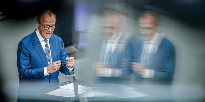 Friedrich Merz spricht im Deutschen Bundestag, er ist zweimal in einer Glasscheibe gespiegelt