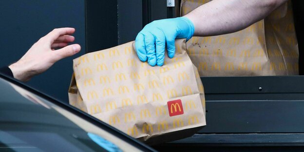 Eine braune Tüte mit McDonalds-Logo wird durch's Fenster in ein Auto gereicht
