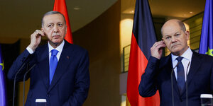Erdogan und Scholz stehen nebeneinander und halten ihr Mikro am Ohr fest