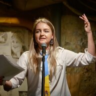 Aljona Mowtschan steht mit einer Krawatte in ukrainischen Farben an einem Mikrophone und gestikuliert, während sie ein Gedicht vorliest.