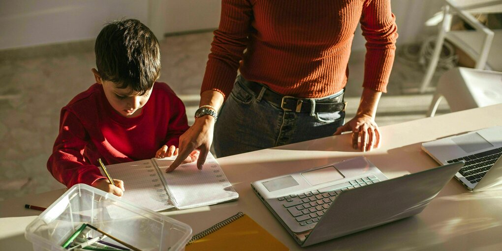 Mutter arbeitet am Laptop neben ihrem Sohn am Esstisch