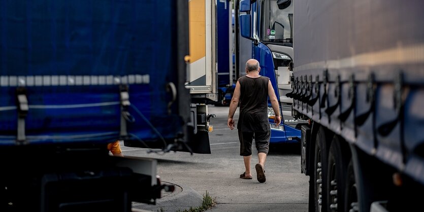 Ein LKW-Fahrer in sommerlicher Kleidung läuft zwischen parkenden Lastwagen