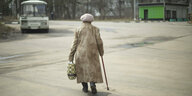 Eine alte Dame läuft mit einem Krückstock auf einer einsamen Straße