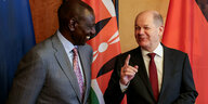 Der kenianische Präsident William Ruto (links) und Bundeskanzler Olaf Scholz (rechts) lächeln sich an, im Hintergrund mehrere Nationalflaggen