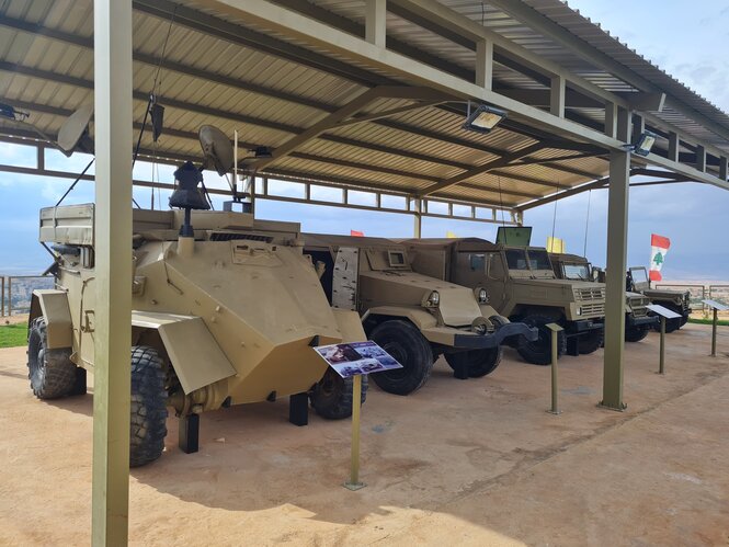 Militärfahrzeuge stehen unter einem Pavillion, im Hintergrund weht die Flagge Libanons