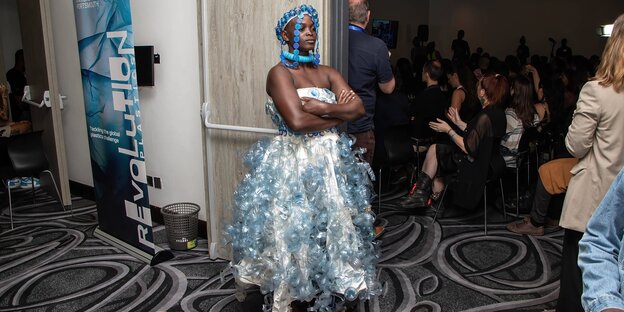Eine Frau steht in einem Konferenzraum und trägt ein kleid, das aus Plastikmüllgemacht ist