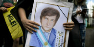 Jemand hält ein gezeichnetes Portrait von Javier Milei in den Händen