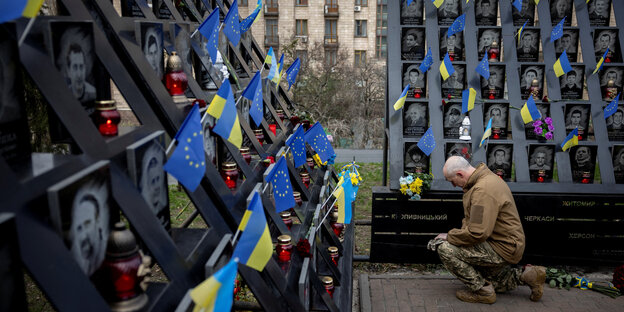 Ein Mann kniet vor Tafeln mit Fotos und ukrainischen Fahnen