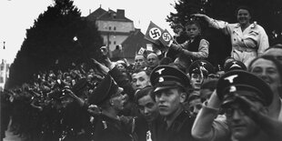 Viele Menschen jublen , manche mit Hakenkreuz-Fähnchen.