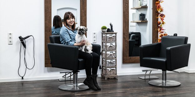 Junge Frau sitzt in einem Friseursalon und hat einen Hund auf dem Schoß