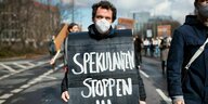 Ein Demonstant steht auf einer Straße - er hält ein schwarzes Schild, auf dem steht: "Spekulanten stoppen"