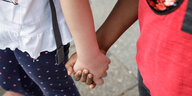 Zwei Kita-Kinder mit heller und dunkler Hautfarbe halten sich an der Hand