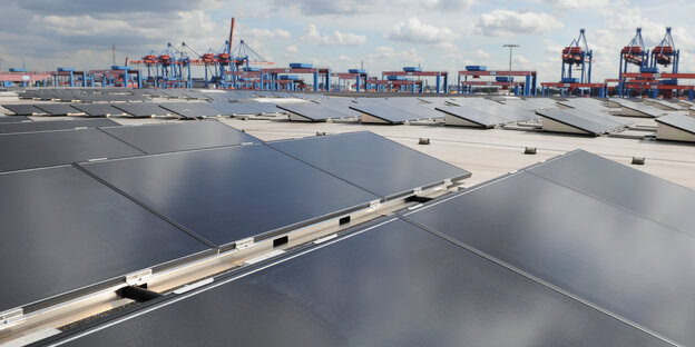 Solaranlagen auf einem Dach, im Hintergrund Hafenkräne