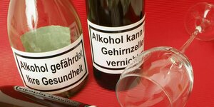 Drei Flaschen Wein mit Warnhinweisen wie: Alkohol kann Gehirnzellen vernichten oder Alkohol gefährdet ihre Gesundheit