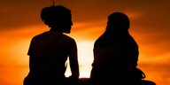 Zwei Frauen sitzen bei Sonnenuntergang auf einer Mauer