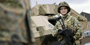 Eine Soldatin steht vor einem Panzer mit Gewehr