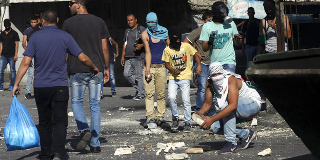 Jugendliche Pästinenser sind vermummt oder tragen Gasmaske. Einer bereitet sich vor, Steine zu werfen