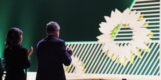 Die Grünen Bundesminister Annalena Baerbock und Robert Habeck applaudieren in Richtung einer großen Sonnenblume auf der Parteitagsbühne