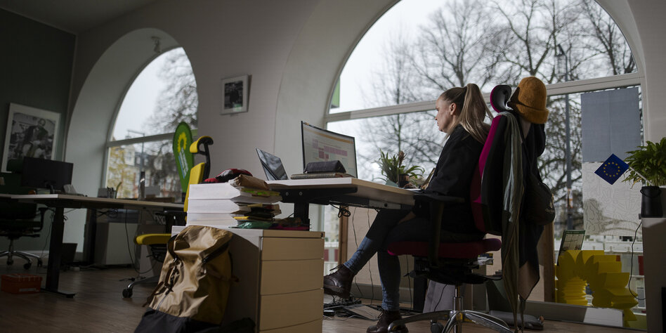 Eine Frau sitzt in einem Büro mit einer runden Glasfassade und arbeitet an einem Computer.