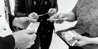 Drei Menschen tauschen Papiere aus, die wie Geldscheine aussehen, Ausschnitt Hände