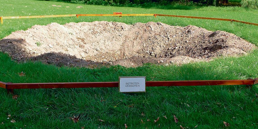 Ein Krater auf einer grünen Wiese. Davor steht ein Schild mit der Aufschrift "Betreten verboten".