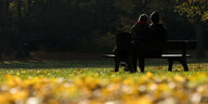 Ein Paar sitzt zwischen gelben Blättern im Volkspark Humboldthain in Berlin auf einer Bank.
