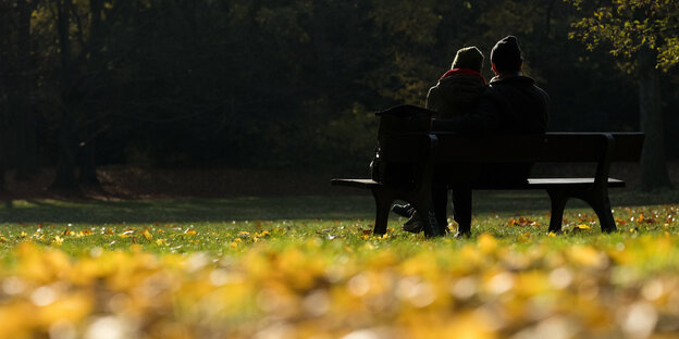 Ein Paar sitzt zwischen gelben Blättern im Volkspark Humboldthain in Berlin auf einer Bank.