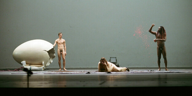 drei Menschen auf einer Bühne, zwei davon nackt.