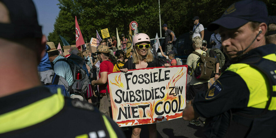Demonstrantin mit Helm und greller Brille in einer Gruppe mit Plakat gegen Kohleabbau in niederländischer Schrift